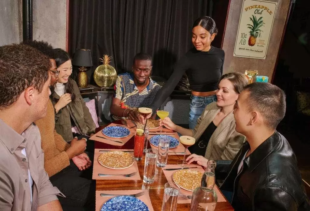 A smiling server in a restaurant serves drinks to a happy group of friends